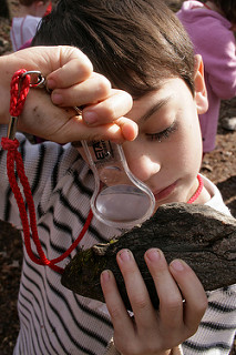 A boy looking at a rock through a magnifying glass